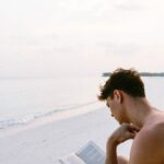 Mand sidder på strand og læser bog